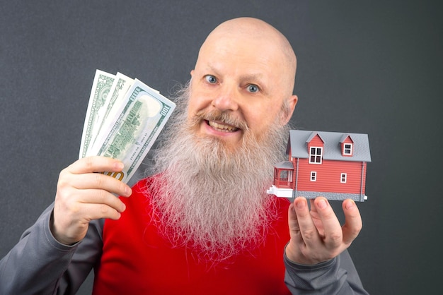 A close-up shot of a person holding a house key with dollar bills wrapped around their finger, symbolizing the correlation between interest rates and the cost of buying a home.