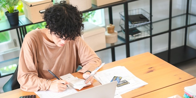 A close-up of a student thoughtfully writing an essay at a desk filled with college application materials, including brochures and a laptop.