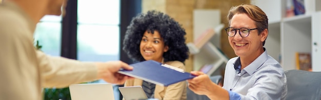 An employee handing paperwork to an HR representative in a modern office setting. The HR representative is smiling and appears helpful.