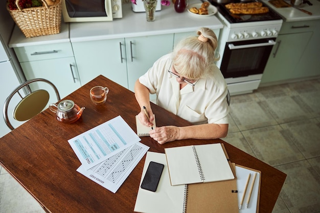 A close-up shot of a homeowner reviewing tax documents at a kitchen table, with a calculator and pen in hand. The scene is illuminated by natural light, emphasizing the importance of careful financial planning and attention to detail.